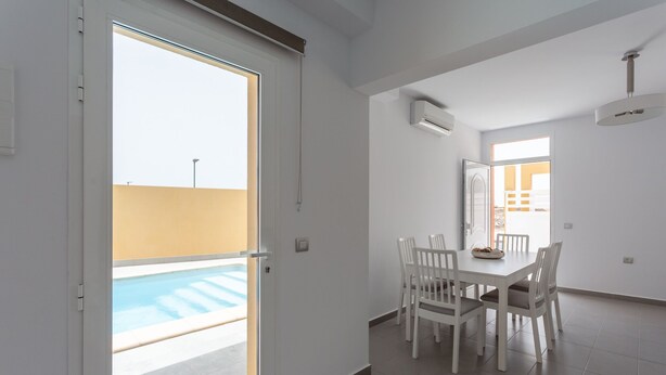 A room with a sliding glass door leading to a pool, a dining area with a table and chairs, and an air conditioning unit on the wall. - BUTTERFLIES POOL 4 TRANQUILITY AND RELAXATION (Puerto del Rosario)