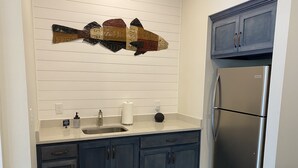 A kitchen with a stainless steel refrigerator, a sink with a faucet, and a countertop with a soap dispenser and paper towel holder.