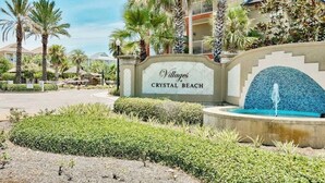 Un letrero que dice 'Villages at Crystal Beach', con una fuente y palmeras al frente.