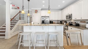 Una cocina amplia con armarios blancos, una isla central con taburetes de bar, electrodomésticos de acero inoxidable e iluminación colgante.