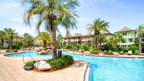 Zona de piscina en un resort, con palmeras, sillas de descanso y una piscina azul cristalina.