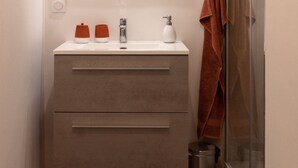 Ein modernes Badezimmer mit einem weißen Waschbecken, einem Spiegel, einem Handtuchhalter und einer Duschkabine.