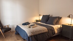 Ein Schlafzimmer mit einem Bett, zwei Nachttischen mit Lampen, einem Sessel und Holzboden.