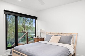 A bedroom with a large window, a bed, a bedside table, and a lamp. - Narani Rise (Fairhaven)