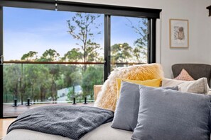 Ein modernes Schlafzimmer mit großem Fenster, einem Bett mit vielen Kissen und einem gerahmten Bild an der Wand.