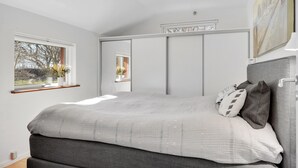 Quarto com cama grande, janela com vista para árvores e um quadro na parede.