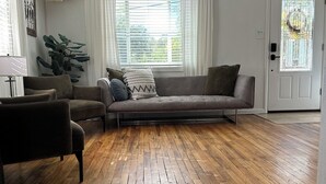 Una sala de estar con un sofá, una silla, una planta grande y una ventana con cortinas.