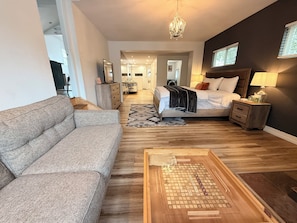 Uma sala de estar moderna com sofá, mesa de centro de madeira, cama com cabeceira, mesa de cabeceira e lustre.
