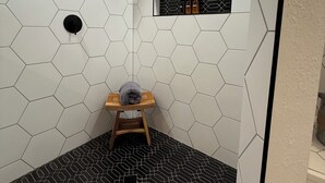 Baño con paredes de patrón hexagonal, un taburete de madera y un estante con botellas.