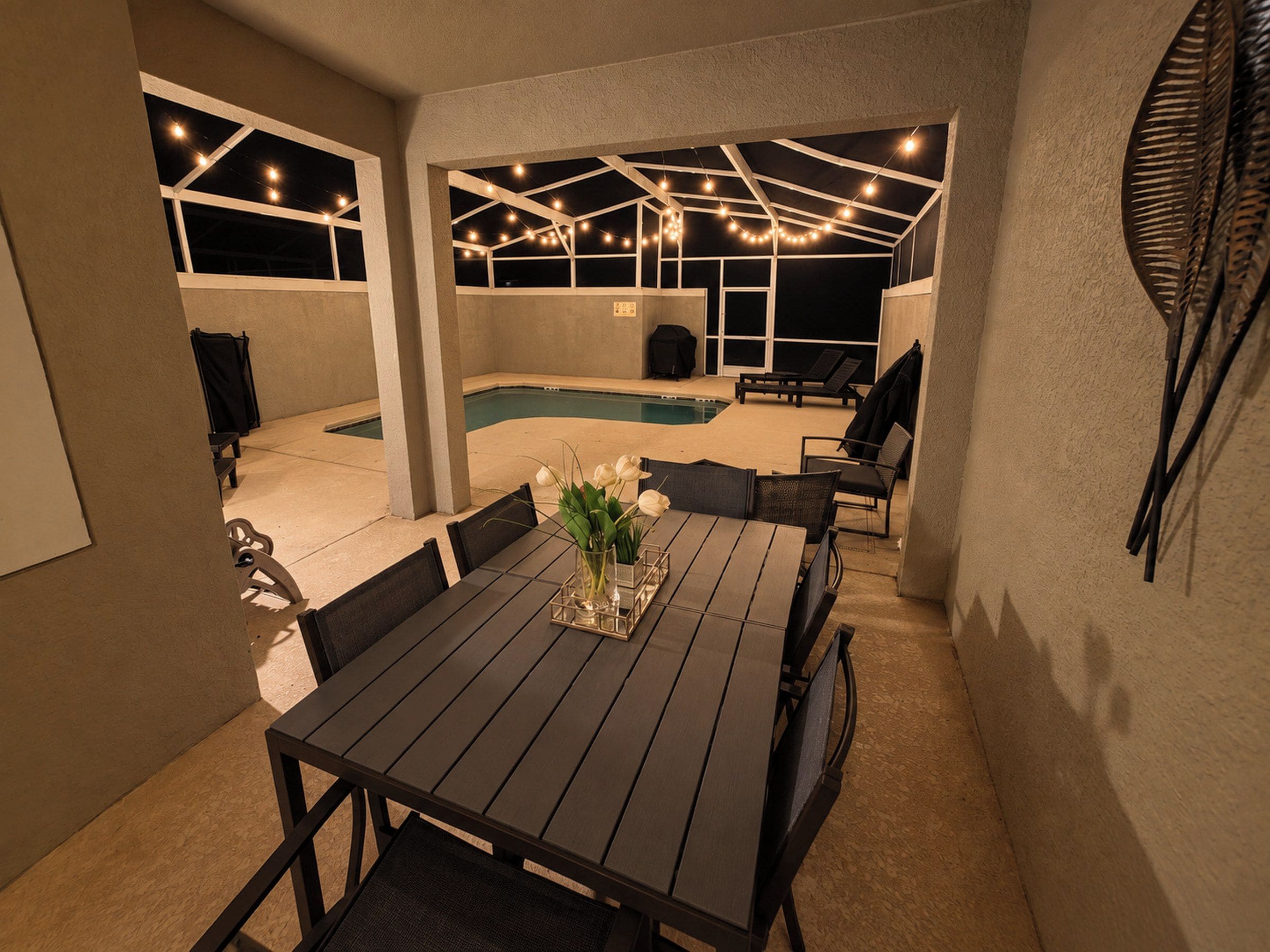 An outdoor patio with a pool, seating area, and string lights.