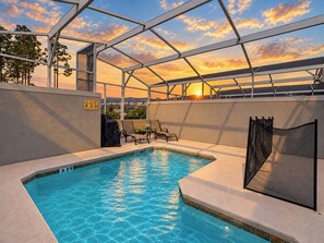 A swimming pool with a glass ceiling, lounge chairs, and a view of the sunset.