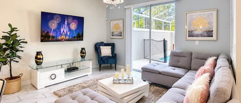 Una sala de estar moderna con una mesa de centro de vidrio, un sofá gris, un sillón azul y un televisor de pantalla plana grande montado en la pared.