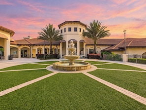 A courtyard with a central fountain, surrounded by well-maintained grass and a building with a tiled roof.