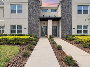 A modern building with a stone facade, numbered doors, and a central entrance with a black overhang.