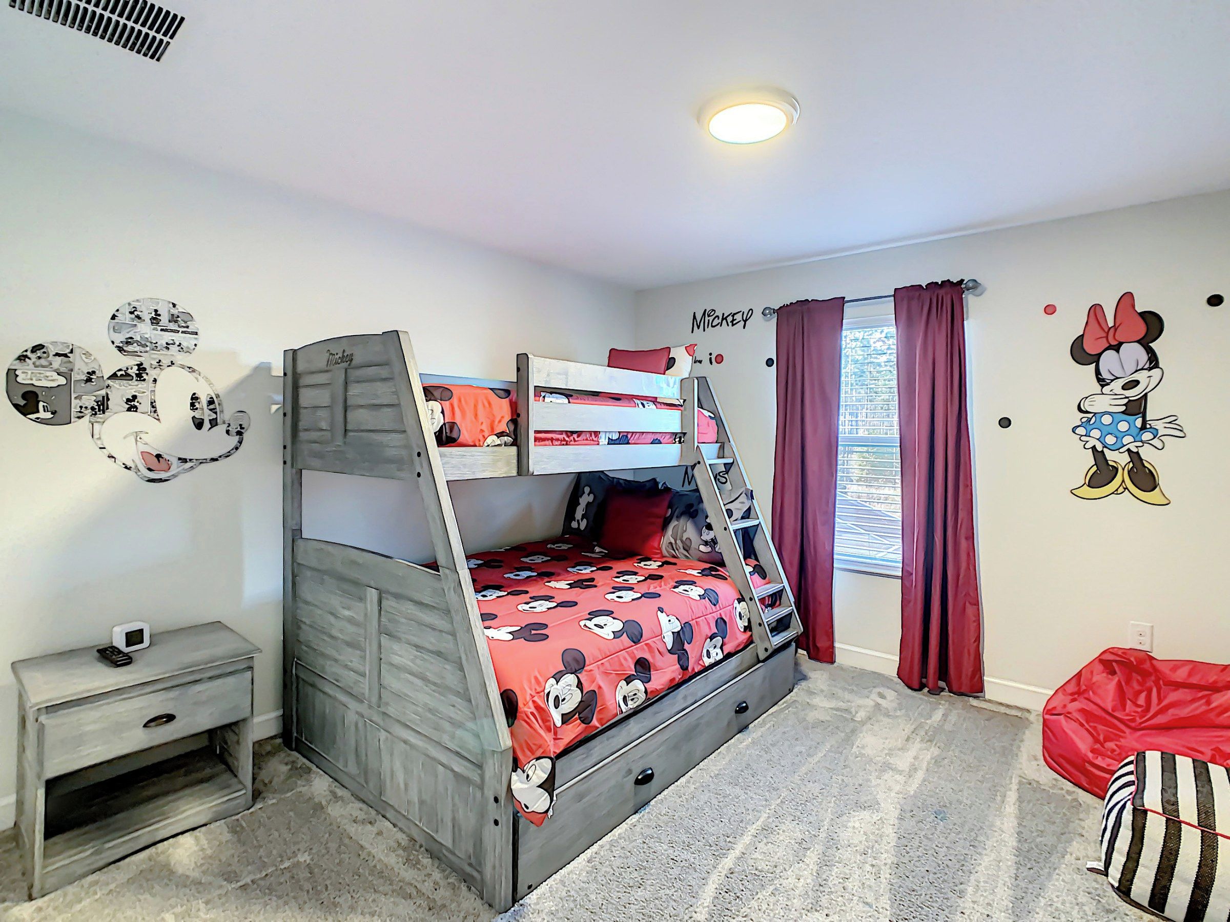 A bunk bed with Mickey Mouse themed bedding, a bedside table with a remote, and a Mickey Mouse wall decal.