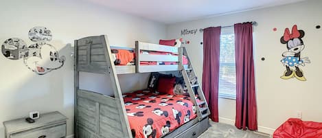 Una cama litera con ropa de cama temática de Mickey Mouse, una mesita de noche con un control remoto y un adhesivo de pared de Mickey Mouse.