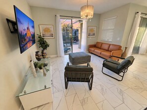 A modern living room with a glass coffee table, a sofa, a chair, and a television mounted on the wall.