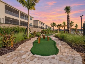 A golf course with a putting green, palm trees, and a building in the background.