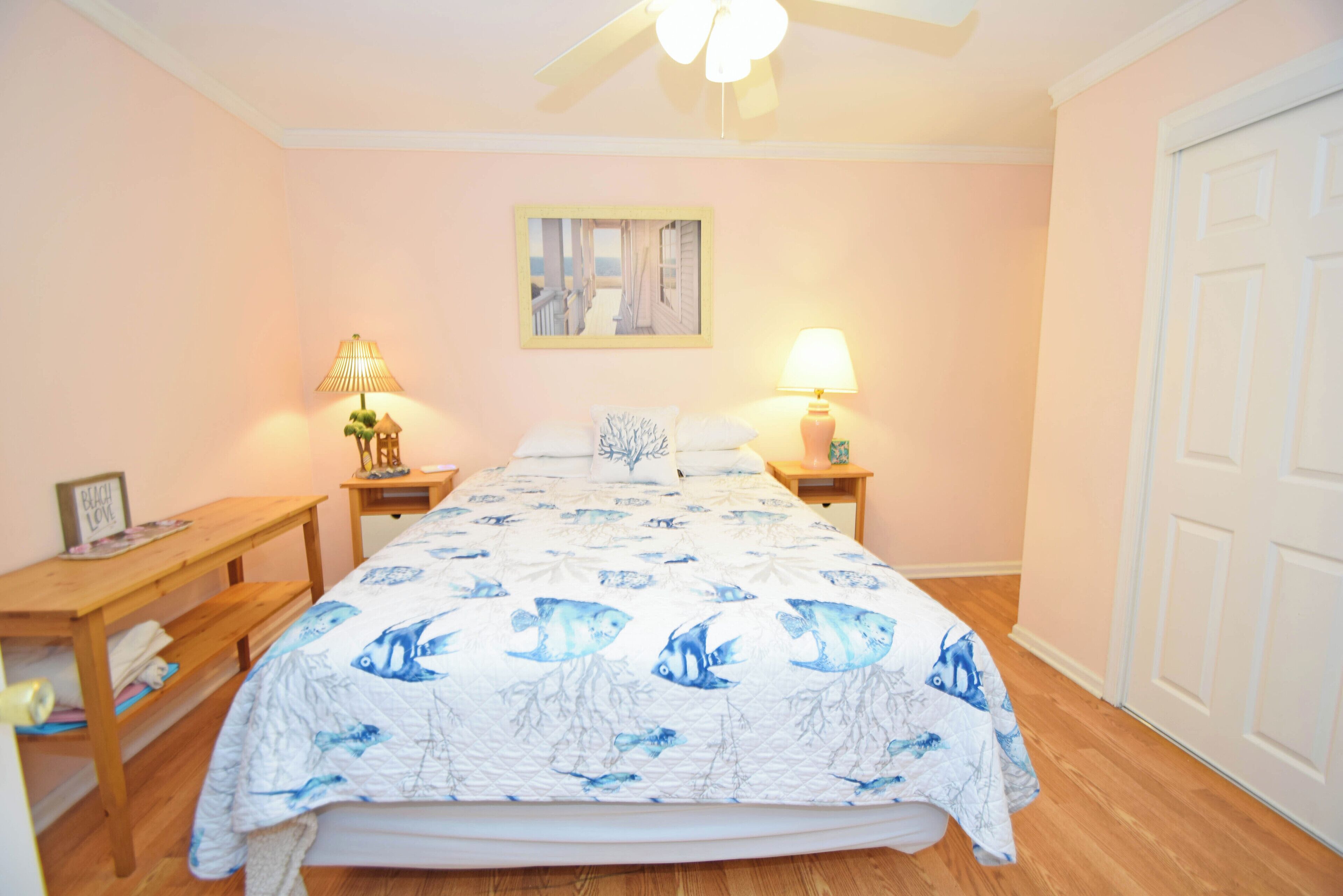 A bedroom with a bed, two bedside tables, a ceiling fan, and a door.