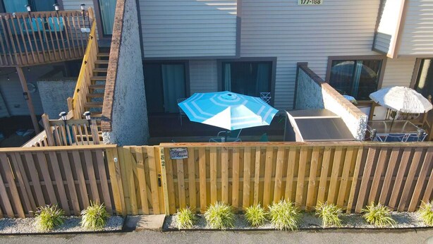 A residential building with a wooden fence, a blue umbrella, and a staircase leading to a balcony.