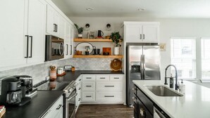 A modern kitchen with white cabinets, a stainless steel refrigerator, and a black countertop. - Brand New and One Block from Magnolia Silos! (Waco)