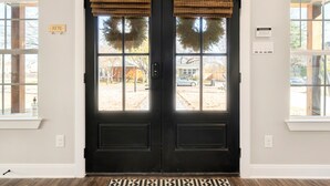 A black double door with a wreath, a 'KEYS' sign, and a thermostat on the wall. - Brand New and One Block from Magnolia Silos! (Waco)