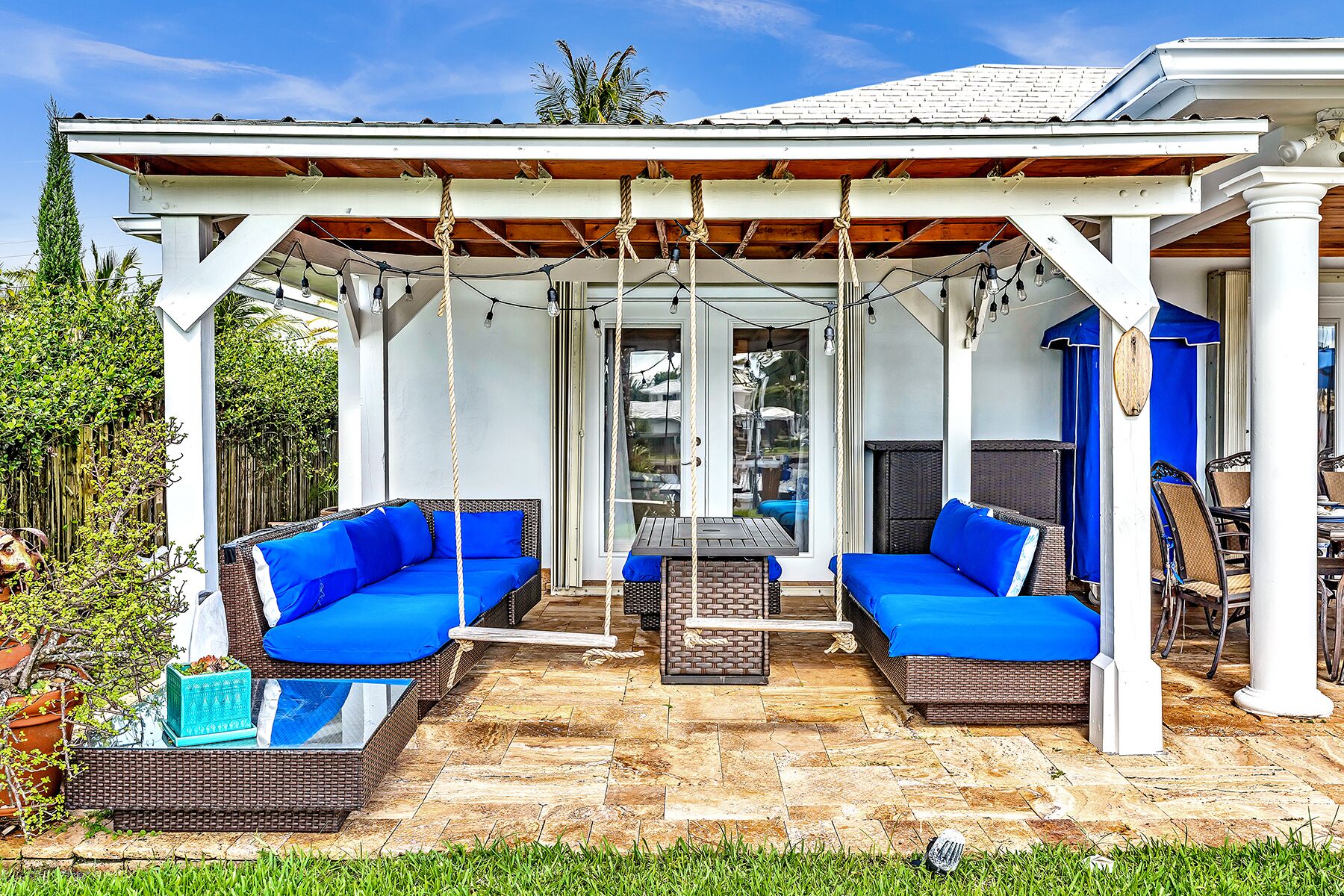 A covered outdoor seating area with two blue cushioned sofas, a small table, and a swing.