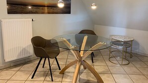 Zona pranzo con tavolo in vetro, quattro sedie, un tavolino rotondo, lampade a sospensione e un dipinto del tramonto alla parete.