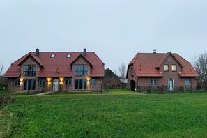 Une grande maison en briques, avec un toit recouvert de tuiles rouges, de nombreuses fenêtres et une pelouse bien entretenue.