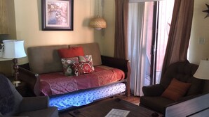 Ein Wohnzimmer mit einer Couch, zwei Sesseln, einem Couchtisch, einer Lampe, einem gerahmten Bild und einer Glastür mit Vorhängen.