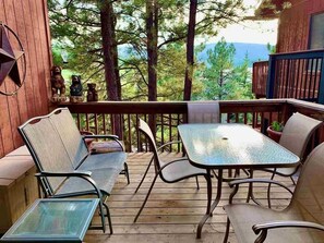 A wooden deck with outdoor furniture, including a table and chairs, overlooking a forested area.