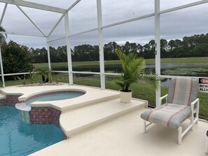 A pool area with a hot tub, a chair, and a view of a golf course and lake.