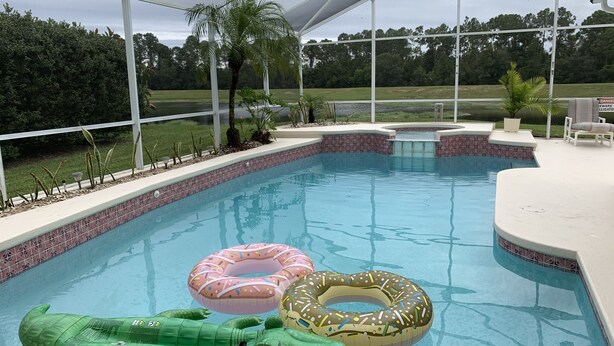 Una piscina techada con borde de azulejos, flotadores inflables y una palmera.