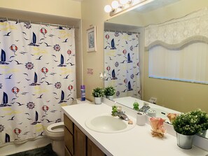A bathroom with a nautical-themed shower curtain, a sink with a mirror, and decorative plants.
