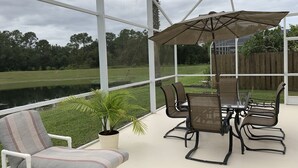 Un patio techado con una mesa y sillas, un sillón acolchado y una planta en maceta.