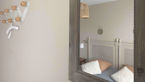 Un dormitorio con un espejo grande, una cama con ropa de cama blanca y marrón, y una lámpara fijada a la pared.