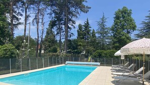 Una piscina rectangular con una solería azulejada, rodeada por una valla y cubierta por un parasol estampado.