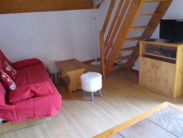 Una sala de estar acogedora con un sofá rojo, una mesita de madera, un taburete blanco y un mueble de madera con un televisor encima.