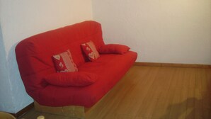 Un sofá rojo con dos almohadones decorativos en una habitación con piso de madera y paredes blancas.