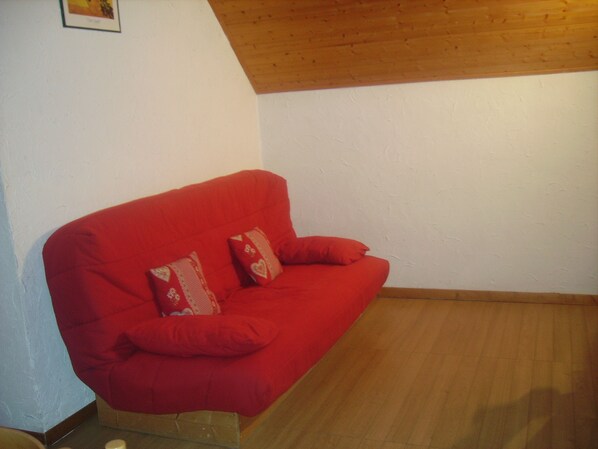 Un sofá rojo con dos almohadones decorativos en una habitación con piso de madera y paredes blancas.