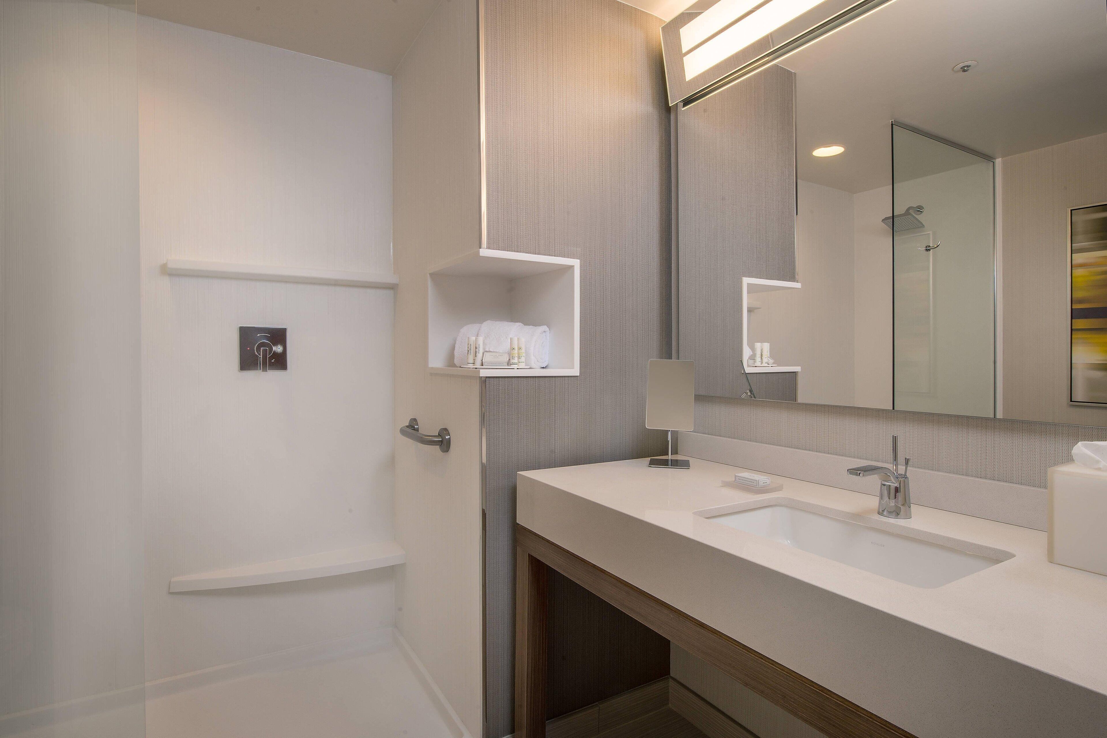 Een moderne badkamer met een grote spiegel, twee wastafels en een douche. Er zijn opbergplanken en een handdoekhouder.