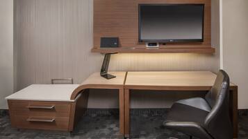 A hotel room with a wooden desk, a black leather chair, a flat-screen TV, and a small speaker.