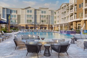 Zona junto a la piscina con sillones de descanso, una fogata y vistas a un edificio de varios pisos con balcones.