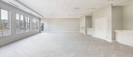 A spacious, well-lit room with large windows, a tiled ceiling, and a clean, neutral color scheme.