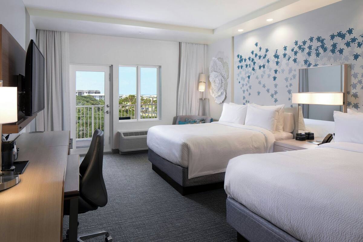 Une chambre d’hôtel avec deux lits, un bureau, une télévision et un balcon avec vue.