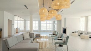 Un salón amplio con un sofá modular grande, varios sillones y una mesa de centro. Hay varias lámparas colgantes de mimbre y un televisor de pantalla plana montado en la pared.