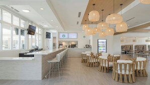 Zona de bar moderna con una barra alargada, taburetes y sillas de mimbre.