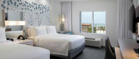 A hotel room with two beds, a desk, a TV, a large window with a view of the sea, and a wall with a floral pattern.