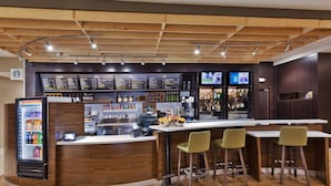 Zona de bar amb sostre de fusta, un dispensador refrigerat de begudes, un quadre de preus i tamborets de bar.