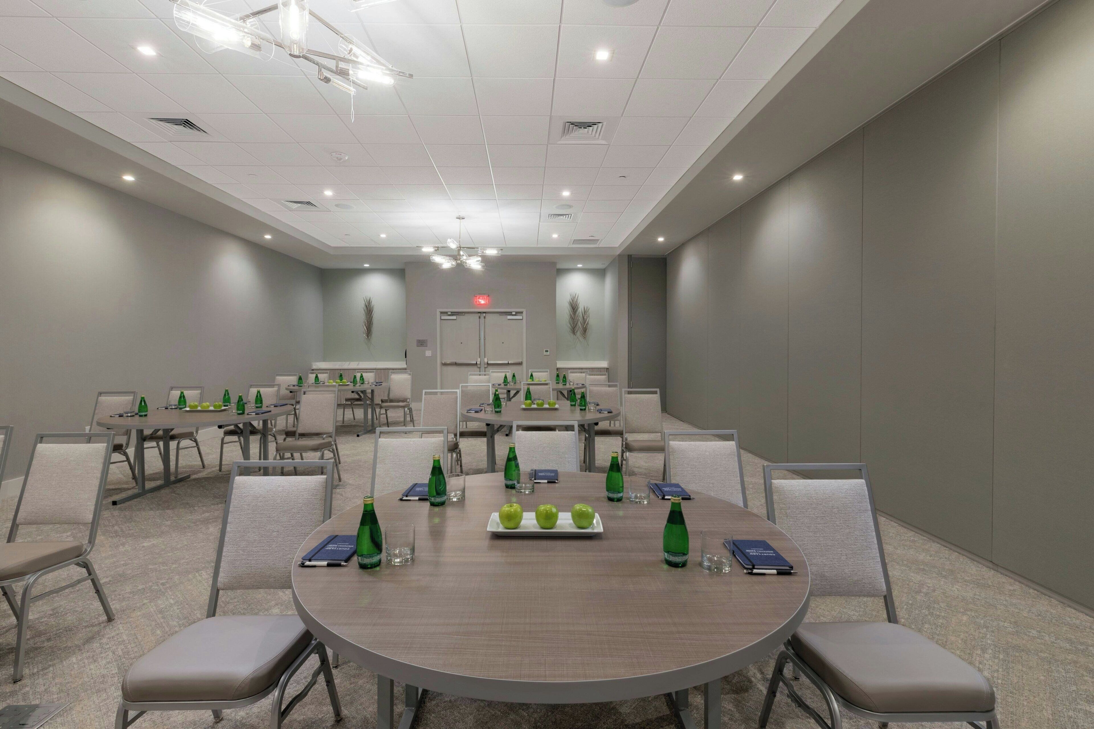 A conference room with round tables, chairs, and green bottles on each table.